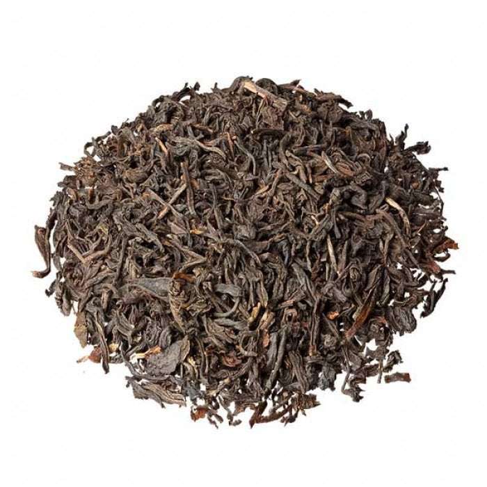 A pile of loose leaf Assam organic tea in a brown paper bag with a transparent flap.