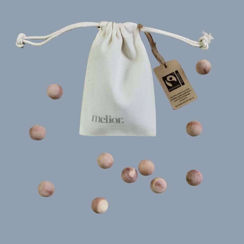 White drawstring bag with 'melior' branding and a tag, surrounded by wooden balls on a light blue background.