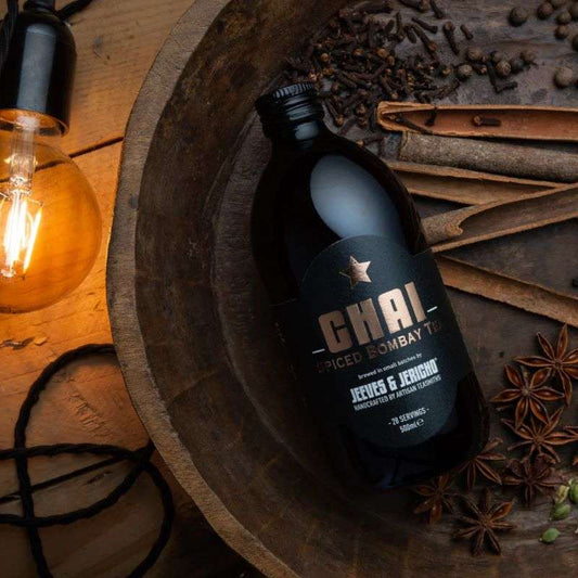 Chai Tea Concentrate bottle surrounded by spices including star anise, cloves, and cinnamon in a rustic setting