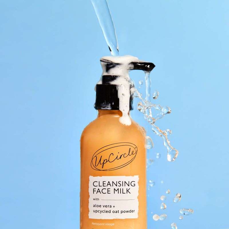 UpCircle Cleansing Face Milk bottle with liquid being poured against a blue background