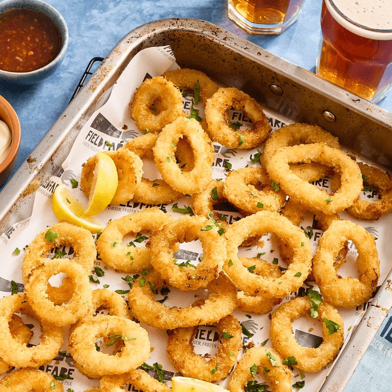 Crispy Calamari rings on a tray with lemon wedges and drinks in the background