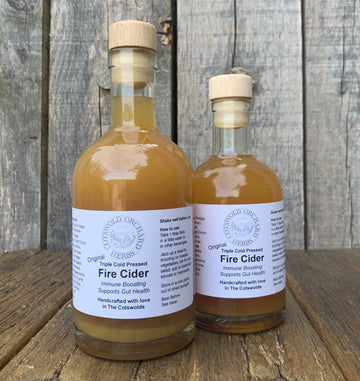 Two bottles of Fire Cider ORGANIC with wooden caps on a wooden surface in natural light