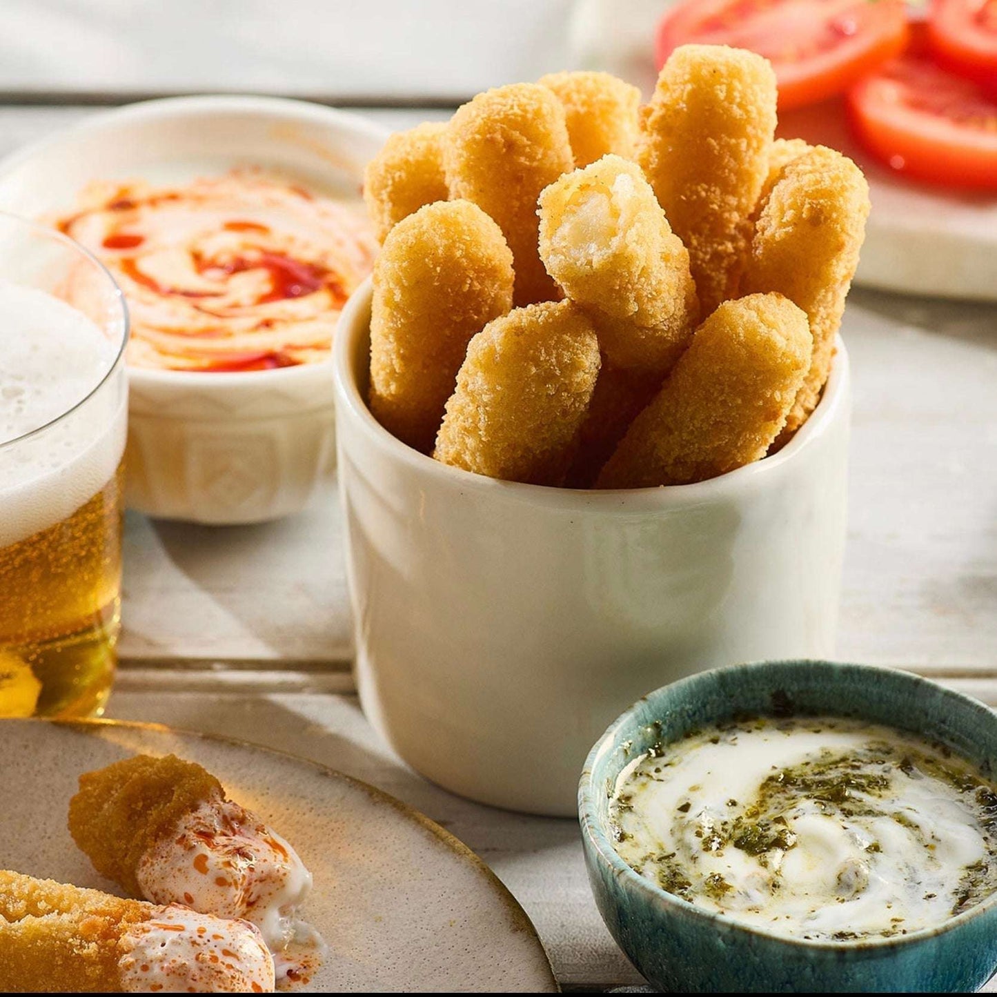 Breaded and fried appetizers in a white bowl with a side of dipping sauce and beer.