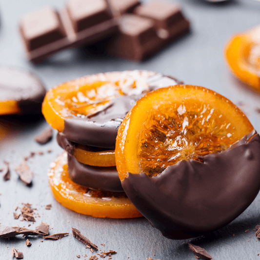 Stack of Candied Orange Slices (per 500g) dipped in rich chocolate with chocolate pieces in the background
