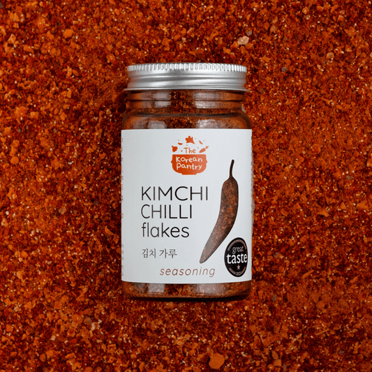 Jar of Kimchi Chilli Flakes (60g) seasoning on a bed of vibrant red chilli flakes, cruelty-free and sustainable.