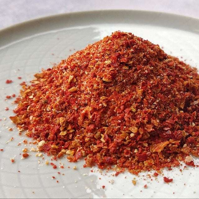 Close-up of vibrant red Kimchi Chilli Flakes (60g) piled on a white plate, ideal for organic cooking.