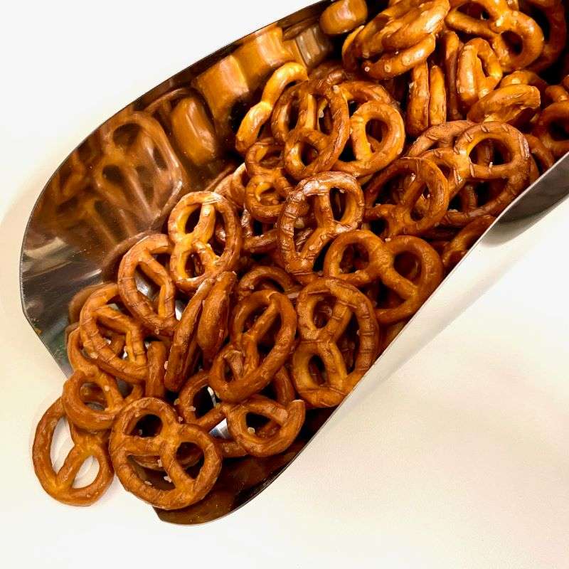 Salted Pretzels (per 200g) spilling from a metal scoop, showcasing crunchy golden brown pretzels.