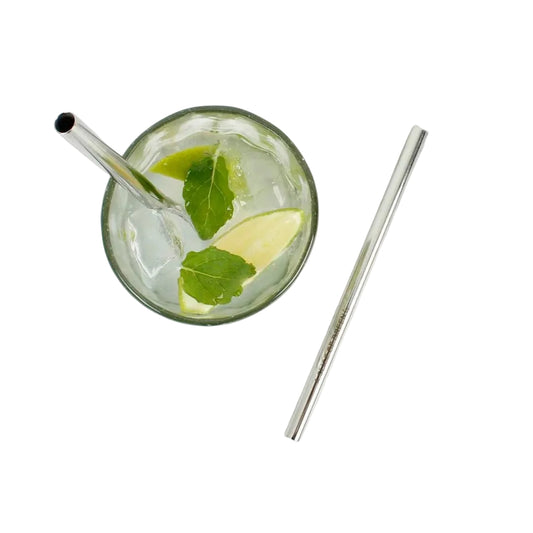 A clear glass with a metal straw containing a clear drink with mint leaves and a lime wedge, placed on a white marble surface next to a second metal straw.