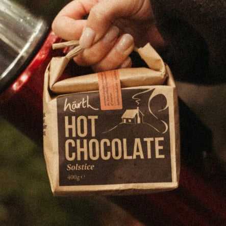 Hand holding a brown paper package of Hot Chocolate ORGANIC (400g) with sustainable, cruelty-free packaging.
