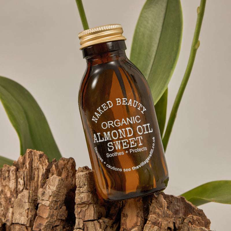 Amber glass bottle of Sweet Almond Oil ORGANIC with gold cap displayed on natural wood and green leaves background