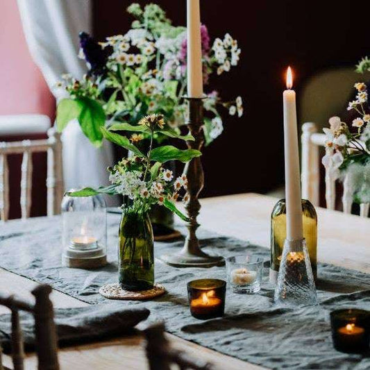 Decorative table setting with candles, flowers, and green bottles on a dark background