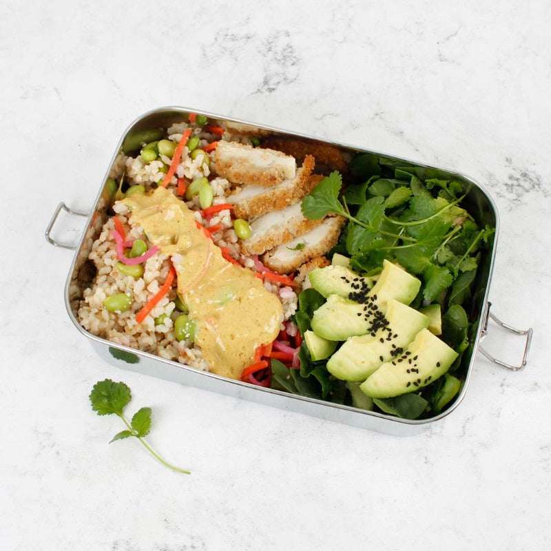 Metal lunch box with a salad and chicken on a white marble surface
