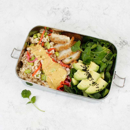 Metal lunch box with a salad and chicken on a white marble surface