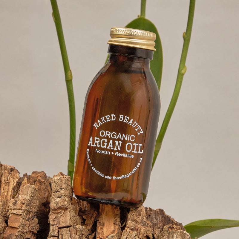 Brown glass bottle of Argan Oil ORGANIC (100ml) standing on bark with green plant stems in background