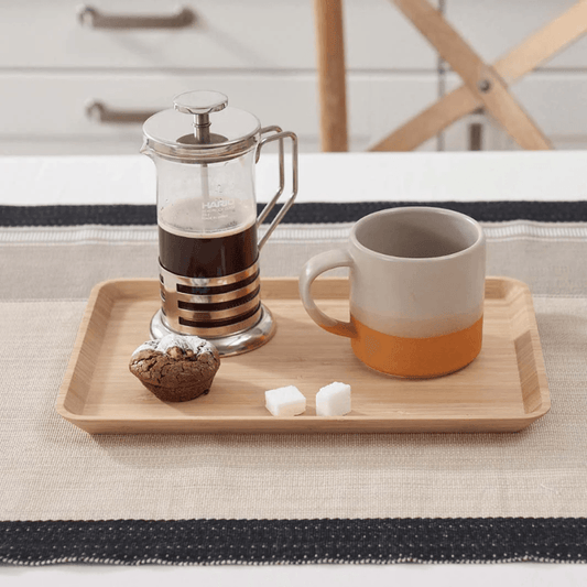 French press with coffee and a mug on bamboo tray on a table.