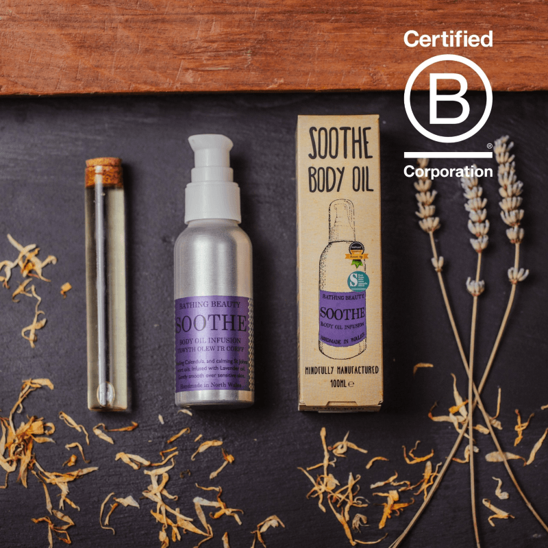 Sooth body oil and packaging on a dark surface with lavender and other herbs, featuring the Certified B Corporation logo.
