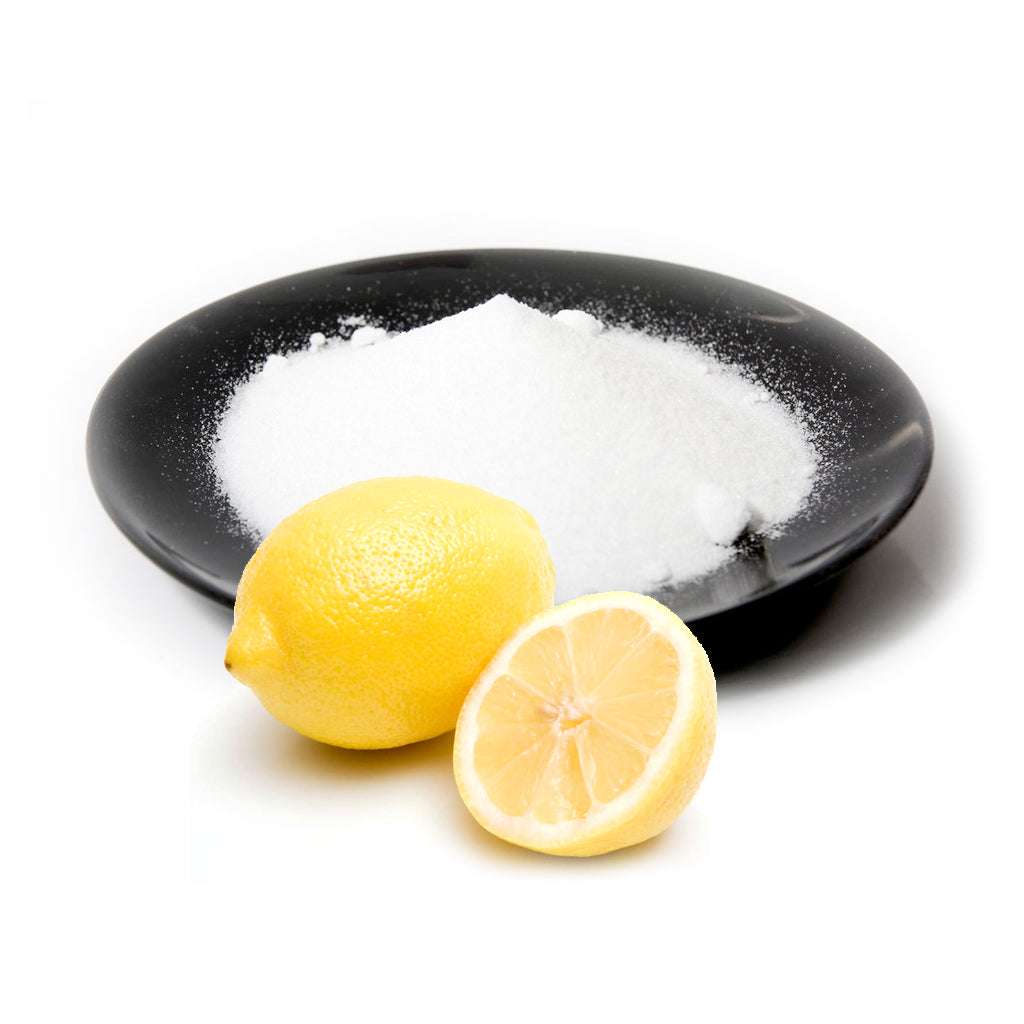 White powder on black plate with fresh whole and halved lemons representing Citric Acid natural ingredient