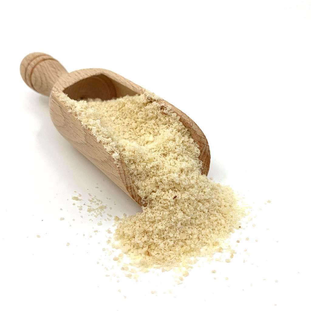 Close-up of a wooden scoop filled with Ground Almond ORGANIC (per 200g) spilling onto a white surface
