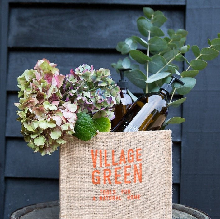Jute bottle bag holding amber glass bottles and fresh flowers for an organic, plastic free refill shop display