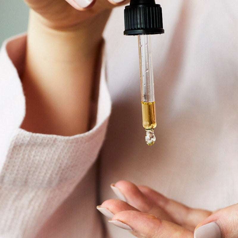 Close-up of a dropper with a drop of liquid held by a person.