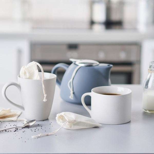 Reusable ORGANIC Tea Bags steeping in white mugs with a blue teapot and loose tea on a kitchen counter