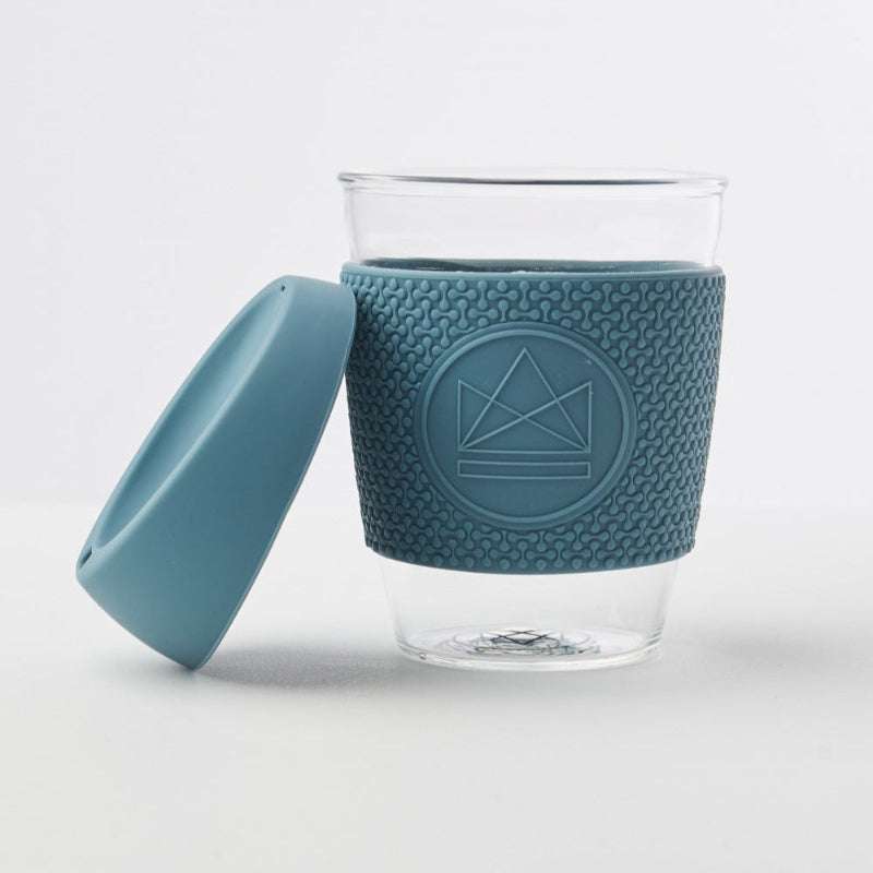 Clear glass cup with textured blue sleeve and matching lid on a white background