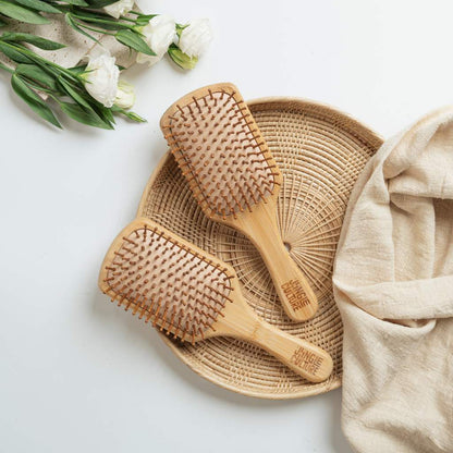Two bamboo hairbrushes on a woven tray with flowers and a towel on a light background