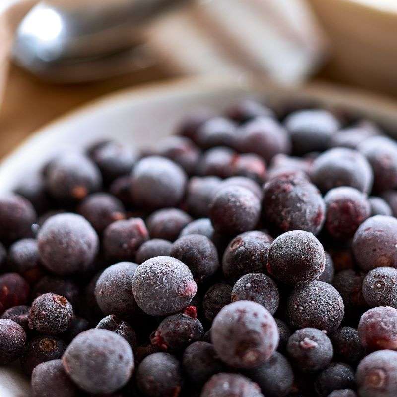 Close-up of frozen black currants in a bowl with a wooden surface in the background