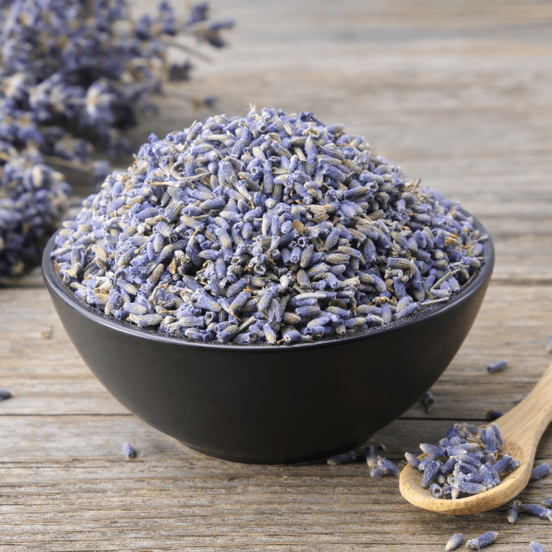 Close-up of dried purple lavender flowers in a black bowl with a wooden spoon on rustic wooden surface, Dried Lavender