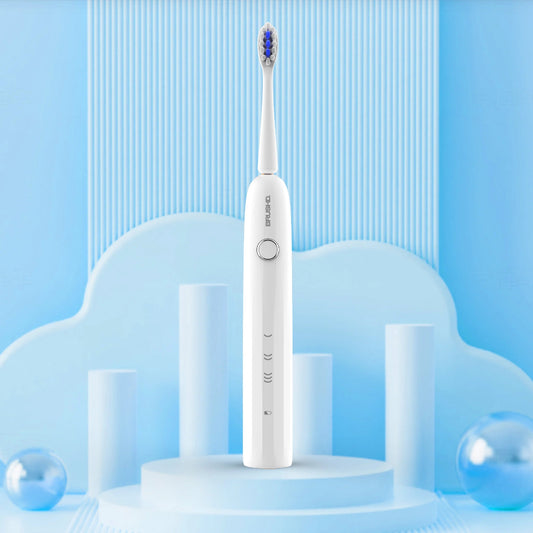 A white electric toothbrush with blue bristles stands upright on a light blue display pedestal. The background is a clean, stylized studio setup with light blue cloud-like shapes, cylindrical props, and subtle blue reflective spheres.