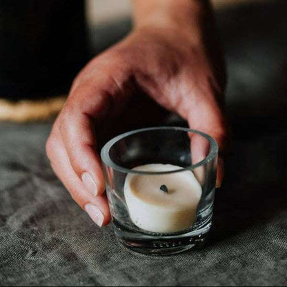 Hand holding a small glass with a candle on a textured surface