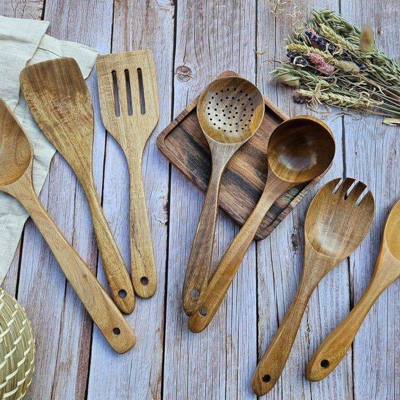 Set of wooden kitchen utensils on a wooden surface with herbs.
