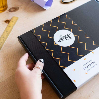 Hand opening a black box with a decorative label on a wooden surface