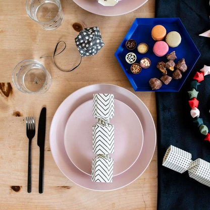 Table setting with pink plates, crackers, and a blue plate of assorted candies on a wooden table.