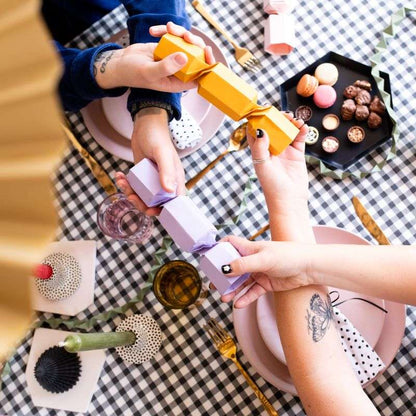 Two hands tearing open a Christmas cracker with a festive table setting in the background.