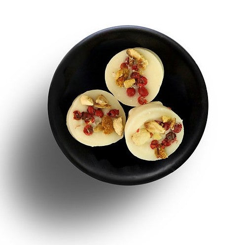 Three white round soya wax melts with dried cranberry toppings on a black plate