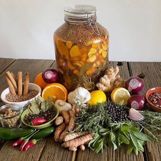 Glass jar of Fire Cider ORGANIC with fresh herbs, garlic, citrus, spices, and natural ingredients on a wooden table