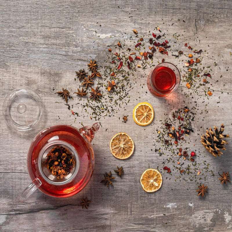 Tea set with a teapot and cup on a wooden surface with dried herbs and oranges.