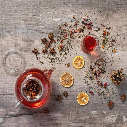 Tea set with a teapot and cup on a wooden surface with dried herbs and oranges.