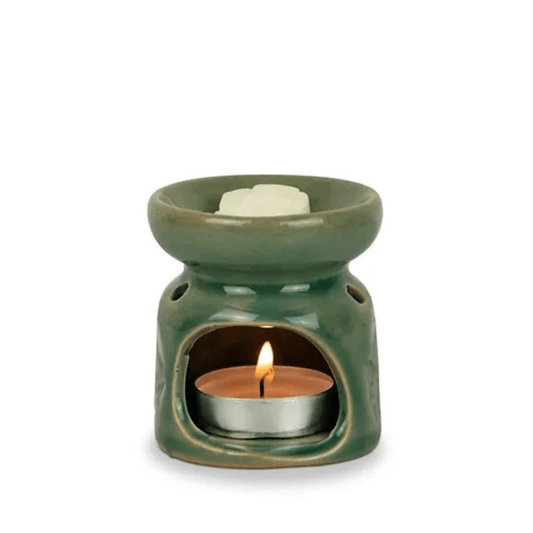 Green ceramic oil burner with a lit candle inside on a white background