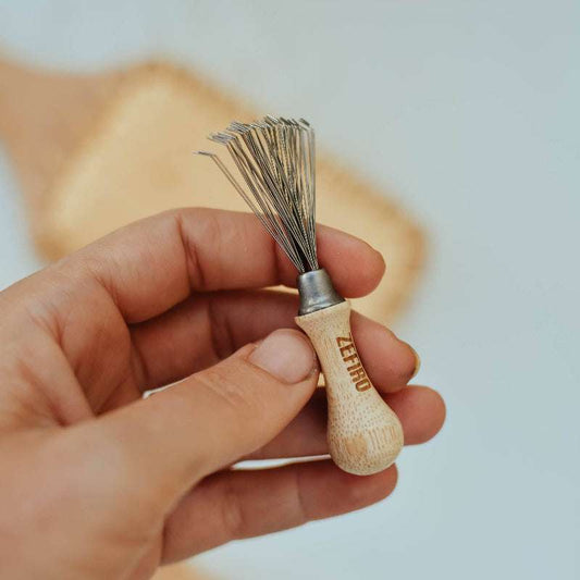 Hand holding a wooden hair brush cleaning tool, brand 'zefiro' visible.