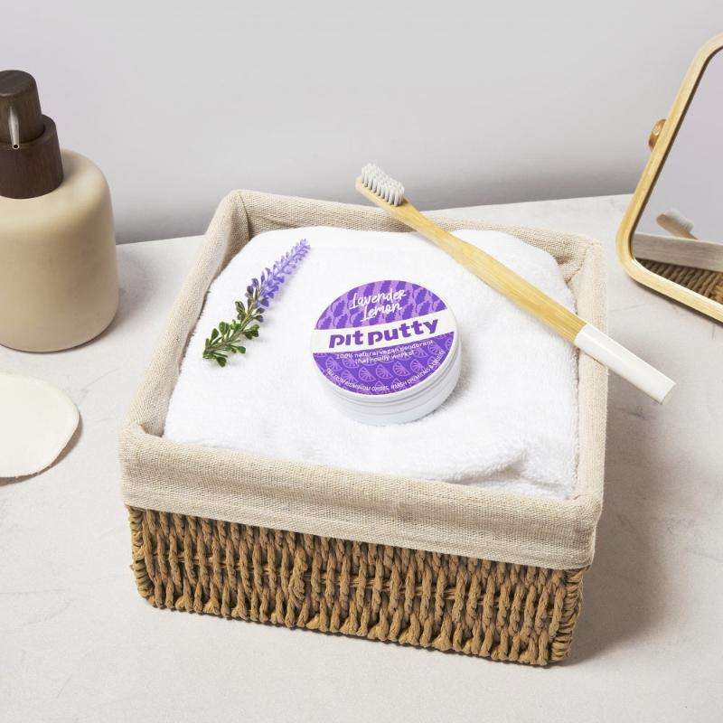 Natural ORGANIC Deodorant in Tin placed on a white towel inside a woven basket with a bamboo toothbrush and lavender sprig nearby