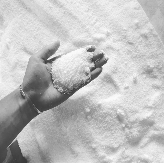 Hand holding white granular Lemongrass Drain Cleaner (per 100g) on a soft textured surface for refill use.