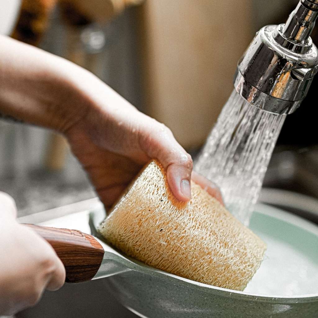 Person washing a sponge under running water from a faucet.
