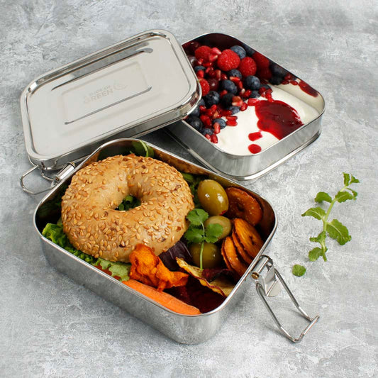 Metal lunch box with a bagel, vegetables, and berries on a gray surface