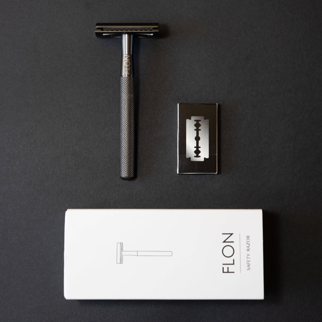 Black safety razor with a blade and FLON packaging on a dark background