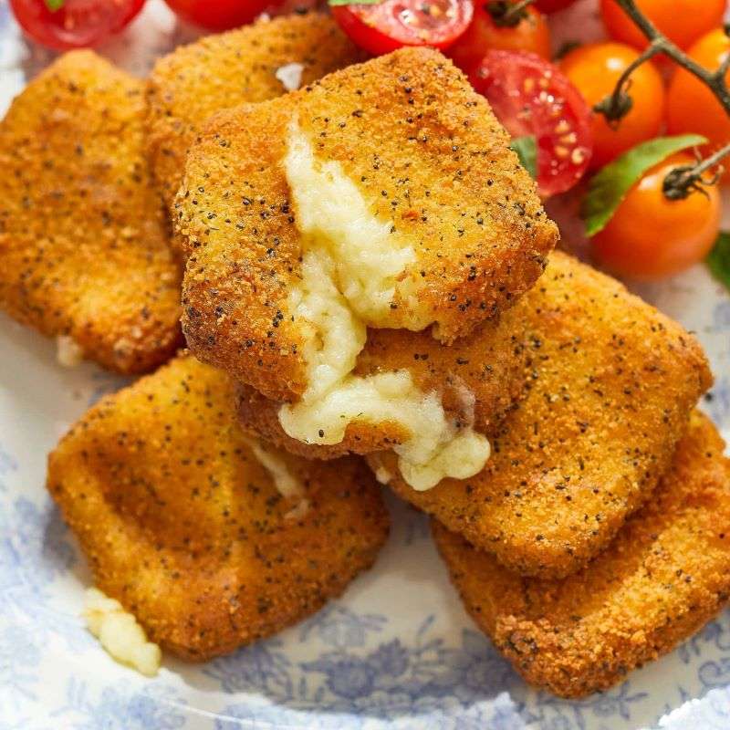 Stack of fried cheese bites  on a plate with cherry tomatoes in the background