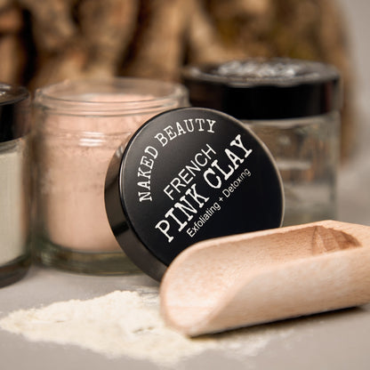 French Pink Clay in a jar with a wooden scoop, natural skincare product promoting exfoliating and detoxing benefits.