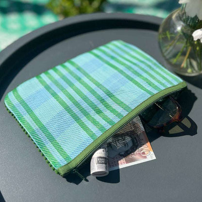 Green and blue striped pouch on a table with sunglasses and money