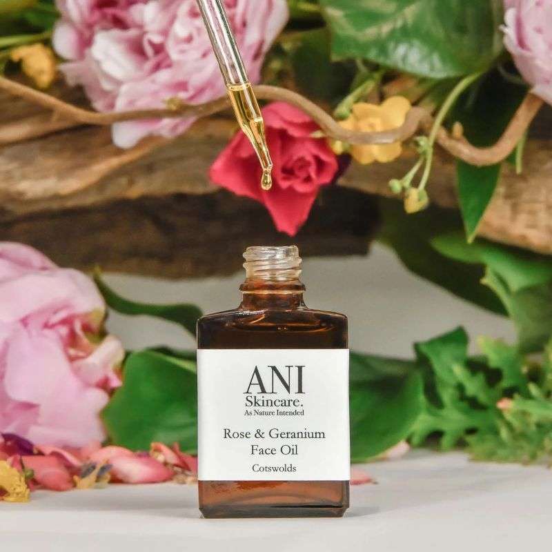 Bottle of ANI Skincare Rose & Geranium Face Oil with flowers in the background